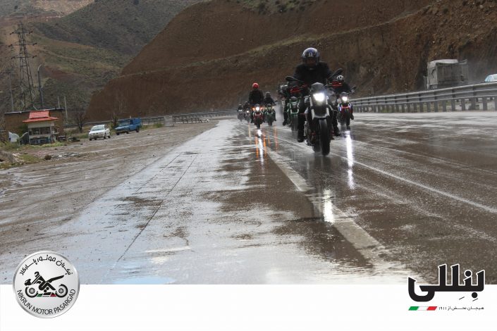 چندین موتورسوار در هوای بارانی روی جاده خیس در حال عبور در آزاد راه هستند.