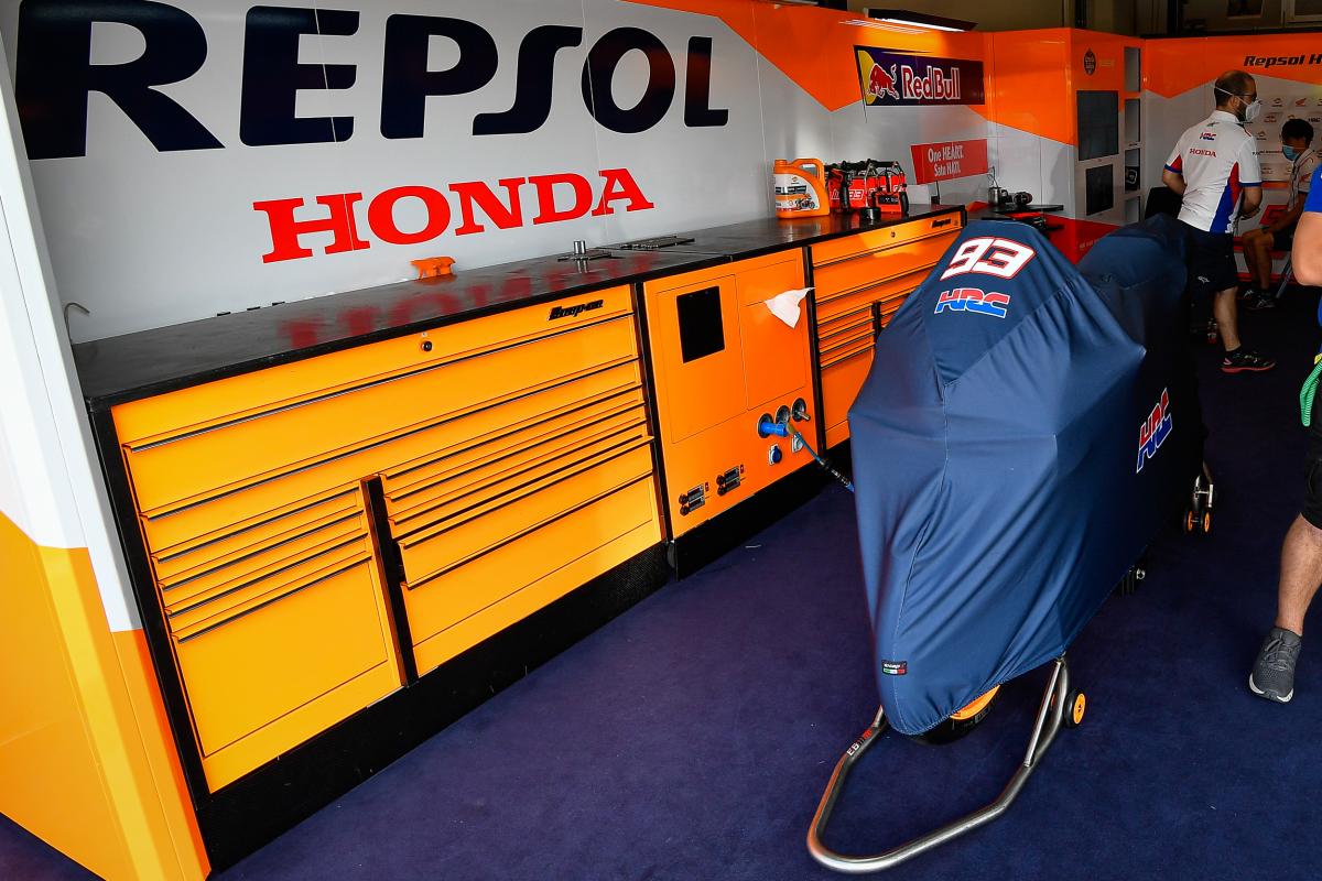 تصویری از فضای داخلی جایگاه تیم هوندا موتور،یک سری کابینت و کشو نارنجی رنگ دیده میشه، یه موتورسیکلت پارک شده که روش روکش کشیده شده که شماره 93 روی آن نوشته شده، دو نفر مسئول فنی  پشت موتور وایساده
